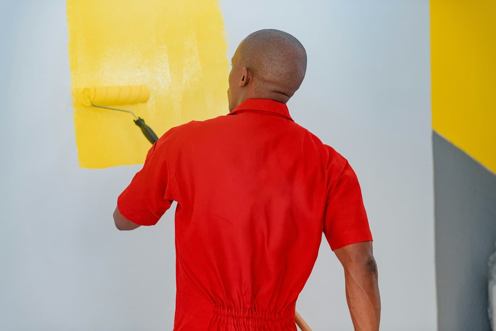 A painter in red overalls rolling yellow paint onto a white wall