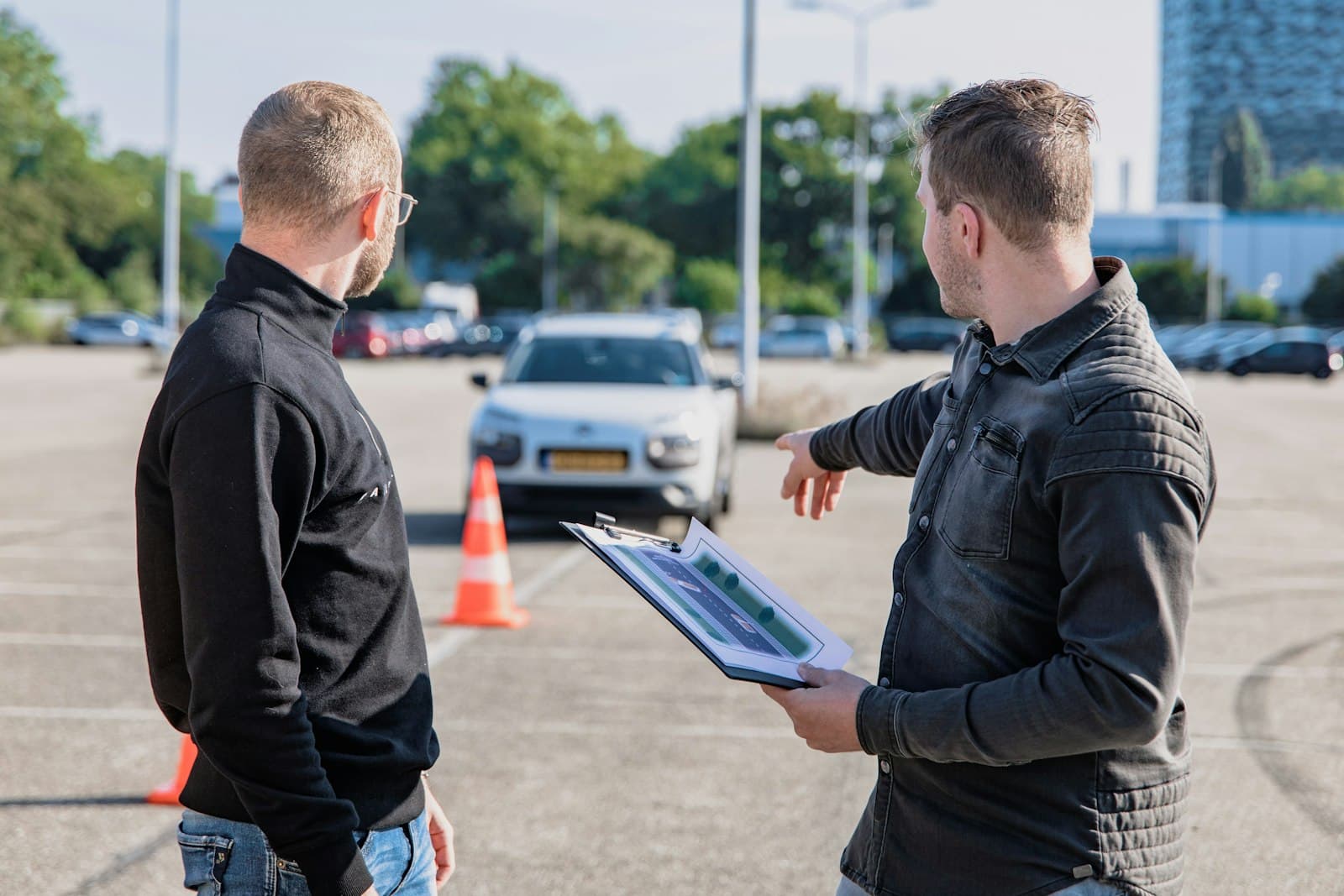 A driving instructor with a clipboard pointing at a car between cones