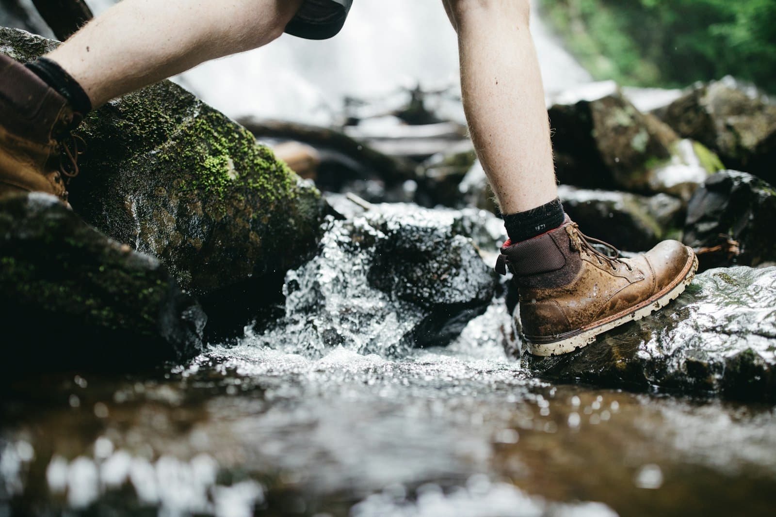 A hiking boot steps across a rocky stream.
