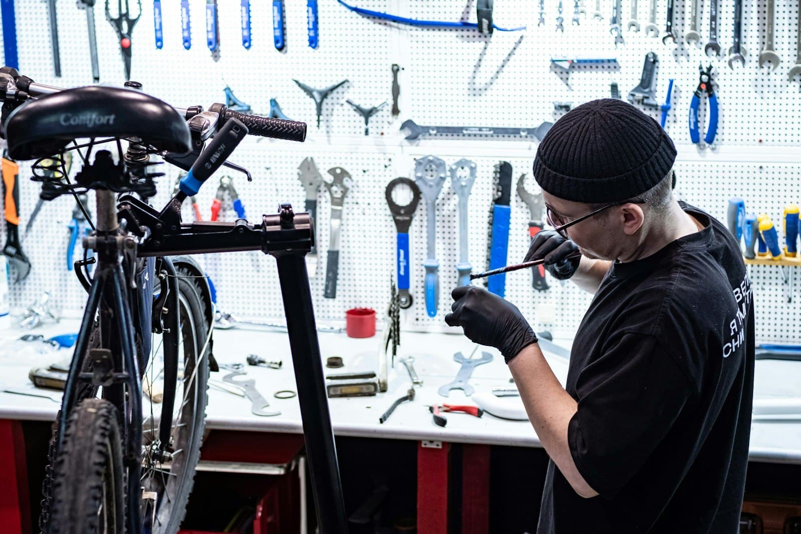 A mechanic works on a bike in front of a wall of tools.