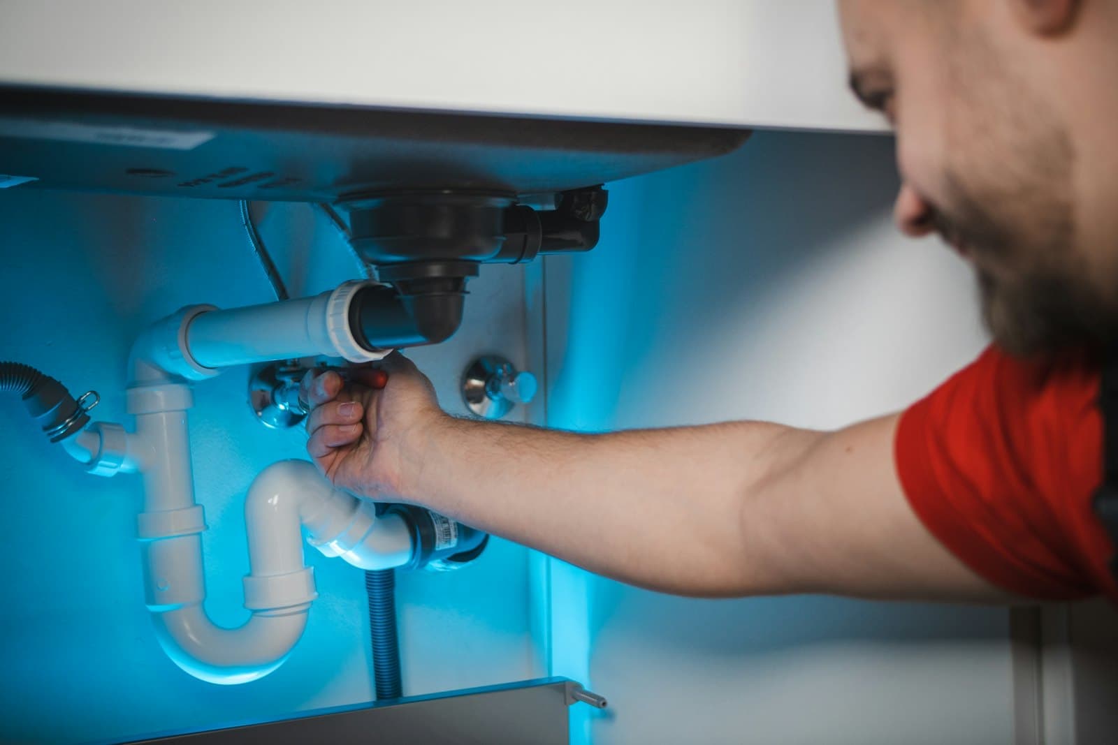 A plumber fixes the pipes under a bathroom sink.