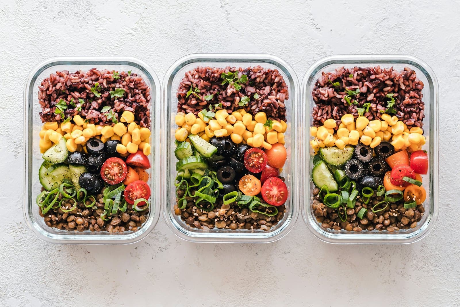 Three meal prep boxes of rice, corn, olives and tomatoes.